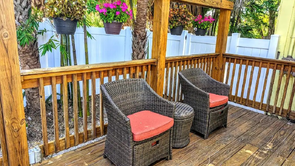 A deck with two couches and flowers hanging on the pillars